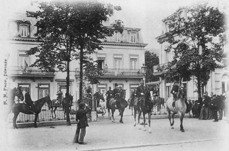 Carte postale (collection privée) : La Reine Marie-Henriette, accompagnée par la Princesse Clémentine, escortée par des gendarmes quitte sa villa spadoise achetée en 1894 (Auparavant Hôtel de l’Avenue et du Midi – Au décès de la souveraine en 1902, le baron Auguste Goffinet hérite de la Villa Royale Marie-Henriette – De 1924 à 1963, la villa devient un lieu de repos pour les coloniaux et est surnommée la « Villa coloniale » – Achat en 1963 par la Ville de Spa dans le but d’y installer les services communaux – En 1965, la Ville renonce à son projet et annonce l’affectation des bâtiments de la Villa Royale : l’aile centrale pour le Musée communal, l’aile de droite pour la Justice de paix, l’aile de gauche pour la police … jusqu’en 2002)